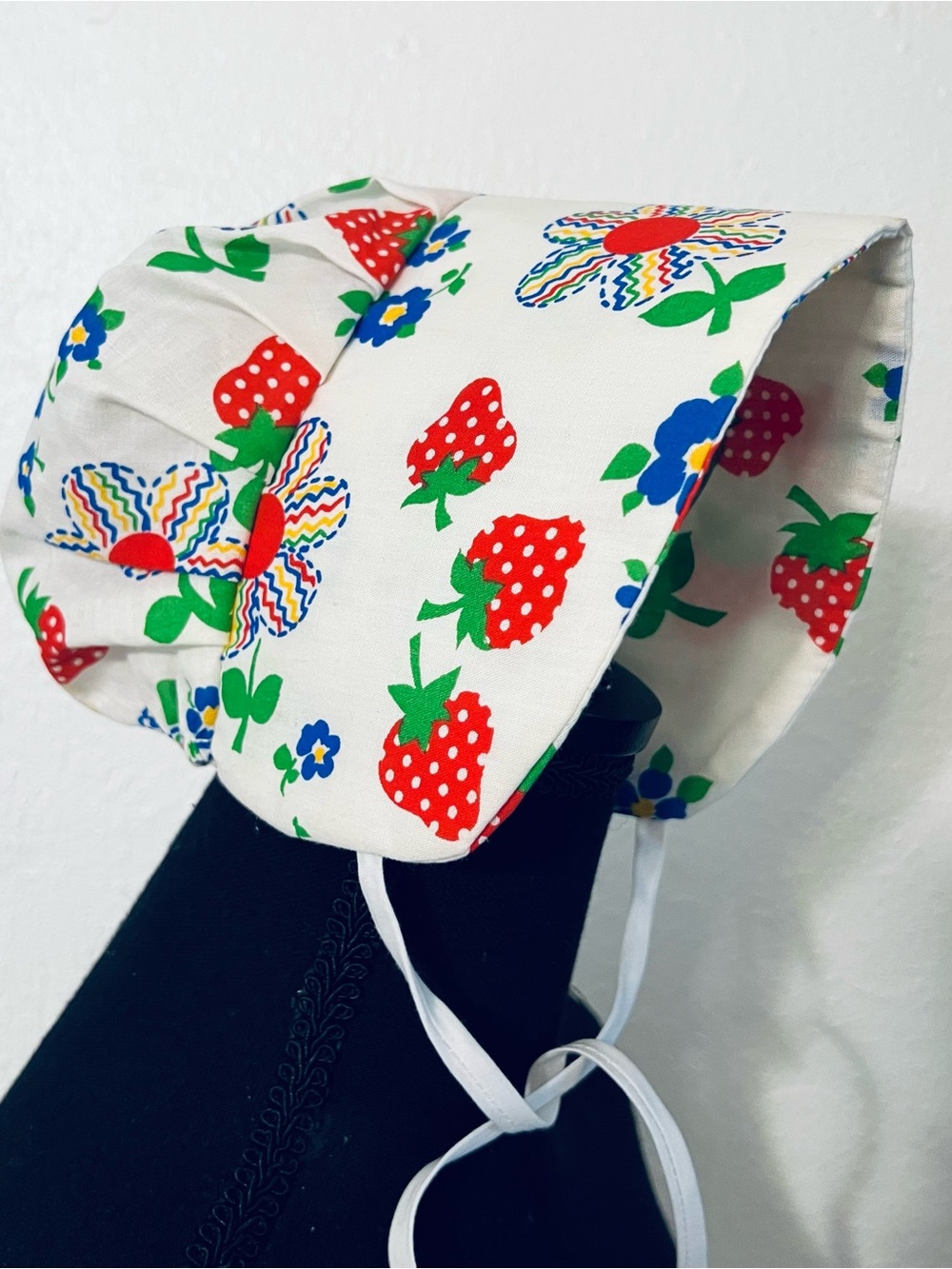 Charming vintage-style baby sunbonnet features a playful white fabric patterned